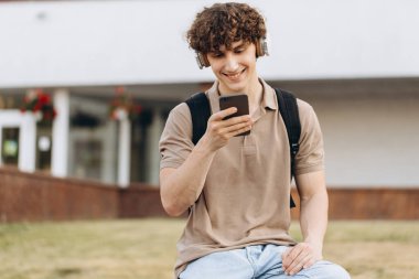 Çekici kıvırcık erkek üniversitesi ya da kampüste telefonla dolaşan üniversite öğrencisi.