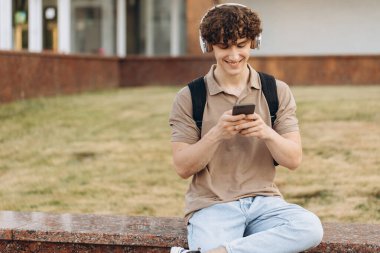 Çekici kıvırcık erkek üniversitesi ya da kampüste telefonla dolaşan üniversite öğrencisi.