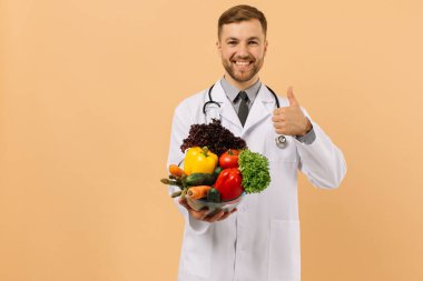 Steteskoplu mutlu erkek doktor beslenme uzmanı bej arka planda taze sebzeler gösteriyor, diyet planı kavramı.