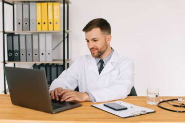 Mutlu erkek doktor iş yerinde dizüstü bilgisayarla otururken internetteki tıbbi web sitesini ya da eğitim seminerini izliyor..