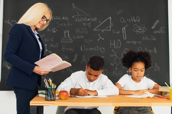 Kvinnlig Lärare Undervisar Skolbarn Som Sitter Vid Ett Skrivbord Och — Stockfoto