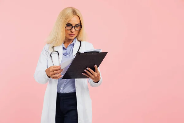 熟女医師で眼鏡とともにStethoscopyスペースとピンクの背景にフォルダを保持 — ストック写真