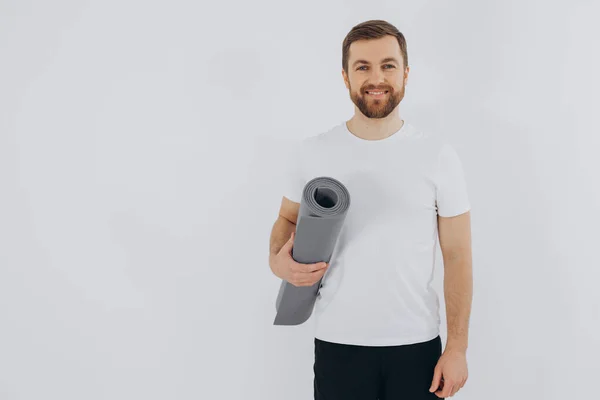 stock image Portrait of handsome bearded man in sportswear holding yoga mat on white background, copy space