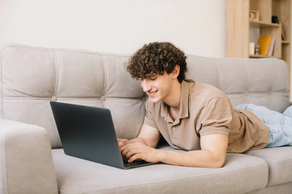 stock image Portrait of attractive young curly hair man lying on the sofa and using laptop