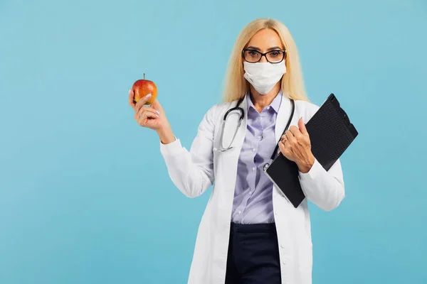眼鏡の熟女医師はリンゴを保持し 青の背景に果物の水を食べることをお勧めします ダイエットと減量の概念 — ストック写真