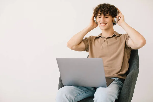 Ελκυστικός Νεαρός Άνδρας Που Χρησιμοποιεί Φορητό Υπολογιστή Φορώντας Ακουστικά Ενώ — Φωτογραφία Αρχείου