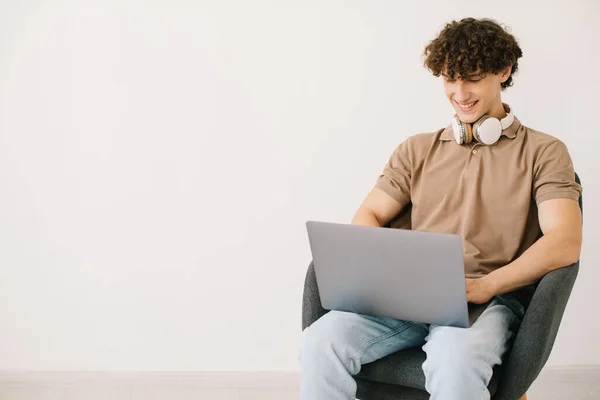 Jovem Atraente Usando Laptop Usando Fones Ouvido Enquanto Sentado Poltrona — Fotografia de Stock