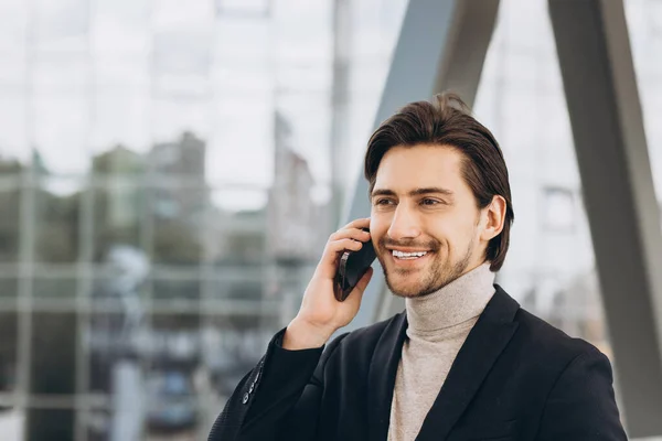 都会の建物やオフィスを背景に電話や笑顔で語るスーツ姿のハンサムな現代男性実業家の肖像 — ストック写真