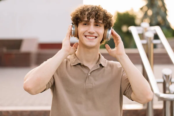 魅力的な巻き毛の男性学生の肖像 スマートフォンで笑顔 — ストック写真