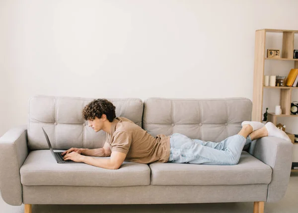 Retrato Atraente Jovem Cabelo Encaracolado Homem Deitado Sofá Usando Laptop — Fotografia de Stock