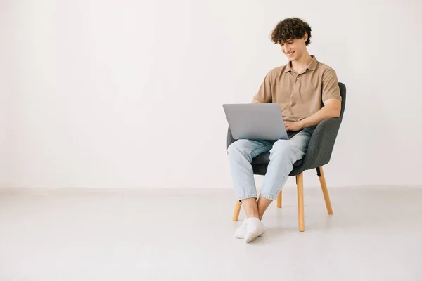 Jovem Feliz Usando Laptop Enquanto Sentado Poltrona Contra Parede Branca — Fotografia de Stock