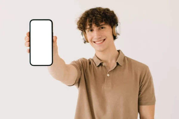 白い画面とコピースペースを持つスマートフォンを保持ヘッドフォンで魅力的な若い男の肖像画 モックアップのための空白の空きスペースを持つプレイリスト — ストック写真