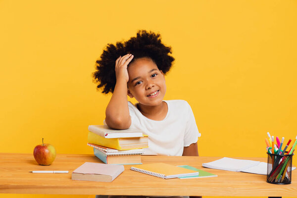 Счастливая афроамериканская школьница делает домашнее задание, сидя за столом. Снова в школу.