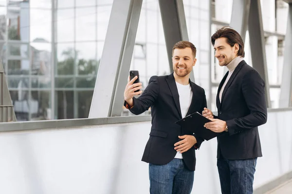 都会のオフィスやビルを背景に自撮りやビデオ通話をする二人の現代のビジネスマン — ストック写真