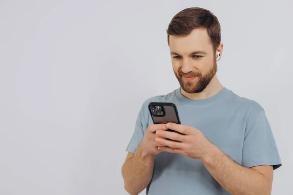 Portret Współczesnego Człowieka Tysiąclecia Brodą Trzymającego Smartfona Słuchającego Czegoś Słuchawkach — Zdjęcie stockowe