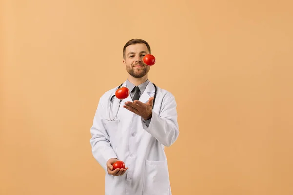 Mannelijke Voedingsdeskundige Arts Met Stethoscoop Glimlachend Jonglerende Tomaten Beige Achtergrond — Stockfoto