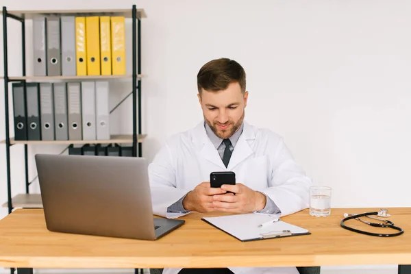 Manlig Läkare Håller Telefon Och Sitter Kontoret Nära Den Bärbara — Stockfoto