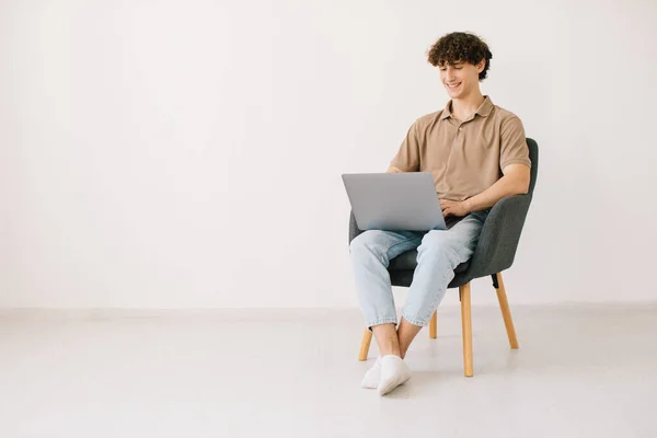 Jovem Feliz Usando Laptop Enquanto Sentado Poltrona Contra Parede Branca — Fotografia de Stock