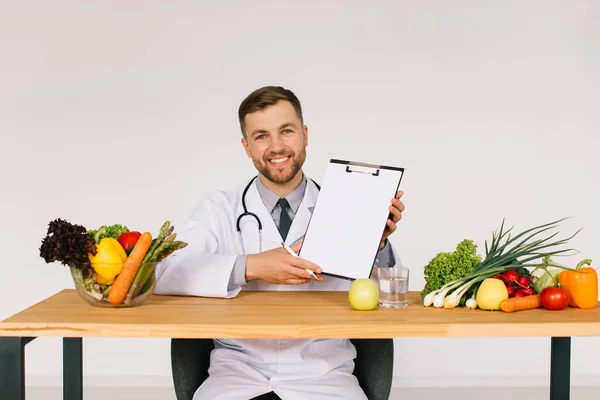 新鮮な野菜の間でオフィスのデスクで職場に座っている幸せな医師の栄養士とコピースペース 食事計画のコンセプトとフォルダを表示 — ストック写真