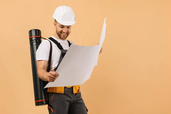 Positive Construction Engineer Examines Drawing Holds Tube Beige Background — Stock Photo, Image