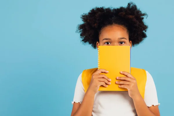 Vtipná Africká Americká Školačka Zakrývající Její Tvář Žlutou Knihou Modrém — Stock fotografie