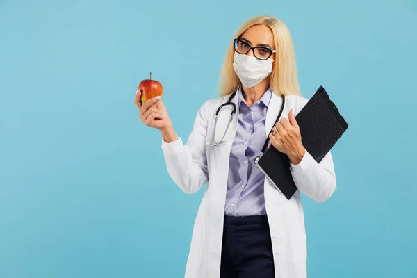 眼鏡の熟女医師はリンゴを保持し 青の背景に果物の水を食べることをお勧めします ダイエットと減量の概念 — ストック写真