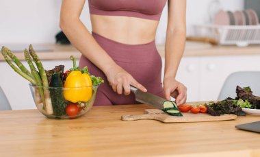 Sportif kadın mutfakta taze sebze salatası hazırlıyor, sağlıklı beslenme konsepti.