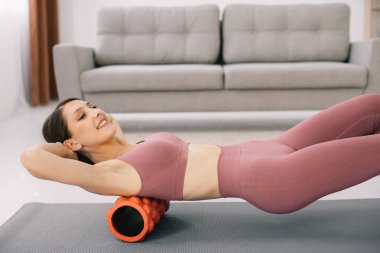 Çekici genç spor kadını evde bir tekerlekle karnına egzersiz yapıyor..