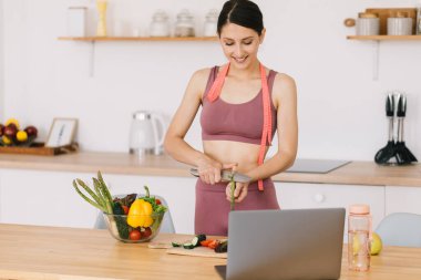 Mutlu spor kadın blogcu portresi kuşkonmaz pişiriyor ve mutfaktaki dizüstü bilgisayarda sağlıklı beslenme konulu video konferansı düzenliyor.