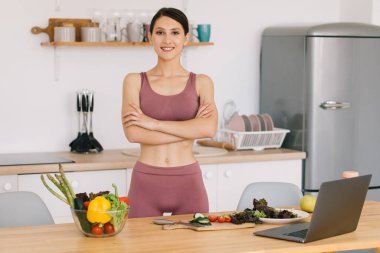 Mutlu spor kadın blog yazarı portresi taze sebzelerle masada, sağlıklı beslenme konseptiyle.