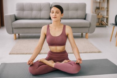 Çekici ve sağlıklı genç bir kadın evde dinlenirken yoga egzersizleri yapıyor.