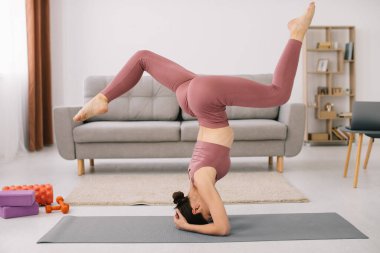 Çekici genç bir kadın baş aşağı duruyor ve evde spor yapıyor..