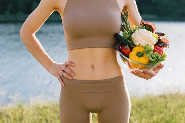 Female vegan holding plate of fresh vegetables near the belly in outdoors