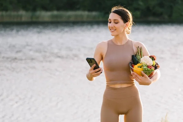 Happy Sporty Woman Looking Phone Holding Fresh Vegetables Outdoors — Stock Photo, Image