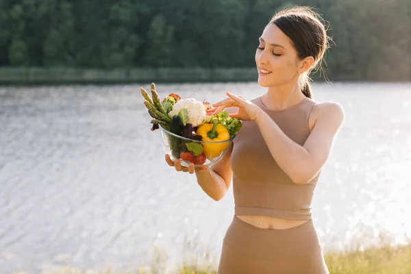 Portrait of happy vegan woman holding plate of fresh vegetables outdoors