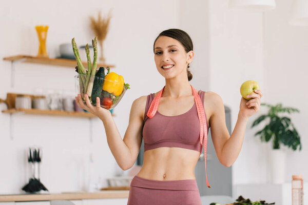 Portrait of happy sporty woman holding apple and plate of fresh vegetables, healthy eating concept