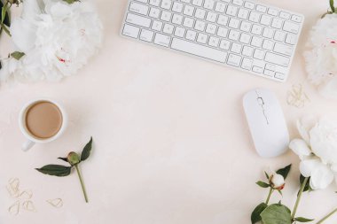 Bir fincan kahve, klavye, şık ofis yazma malzemeleri ve pastel bir tepsi üzerine sahip kadınsı çalışma alanı.