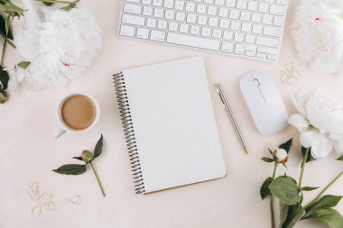 Kadınsı çalışma alanı, boş not defteri ve bir fincan kahve, süt, klavye, şık ofis yazma malzemeleri ve pastel bir masa üzerine.