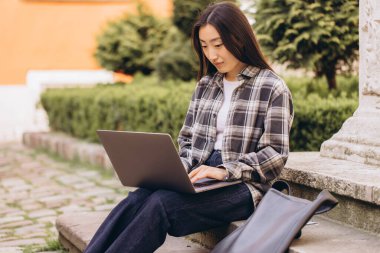 Çalışmak için dizüstü bilgisayar kullanan genç Asyalı bir kadın. Gündüz açık havada oturmak. Modern teknolojiye sahip şehir halkı yaşam tarzı.