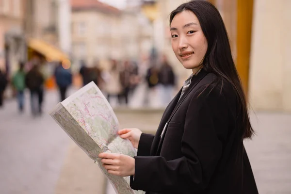 Portrait of a beautiful Korean woman holding a map on the streets of an old European city. Asian woman tourist or business lady traveling in Europe.
