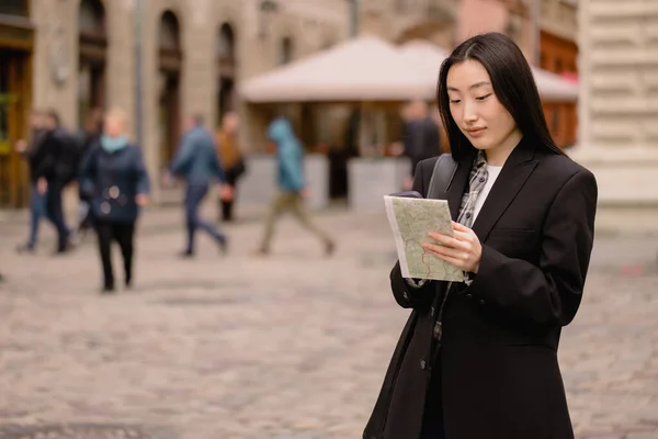 地図やスマートフォンのナビゲーションで方向を確認しながら ヨーロッパの古い街の通りにカジュアルな服で若い幸せなアジアの女性の観光客を肖像画 — ストック写真