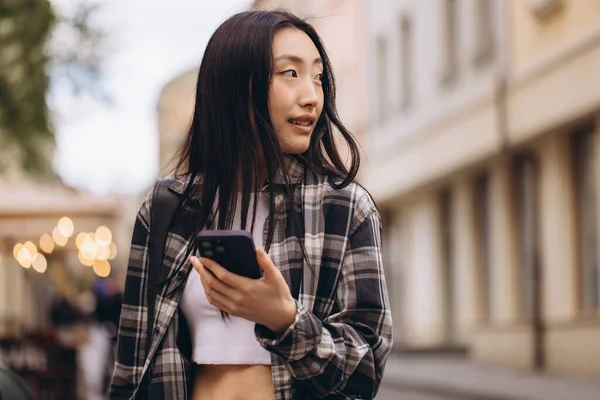 一个漂亮的黑发韩国女人带着智能手机站在古城街道上的画像 — 图库照片