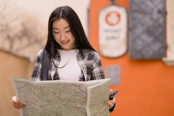 一个美丽而快乐的黑发韩国女人的画像 她手里拿着一张旧城街道上的地图 在欧洲旅行的亚洲女游客 — 图库照片