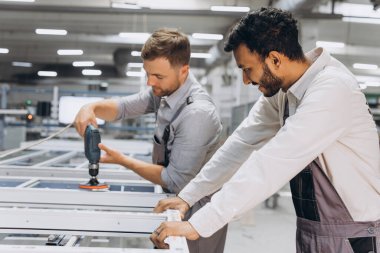 İki erkek uluslararası işçi alüminyum PVC pencere ve kapı üretimi için bir makinede birlikte çalışıyorlar.