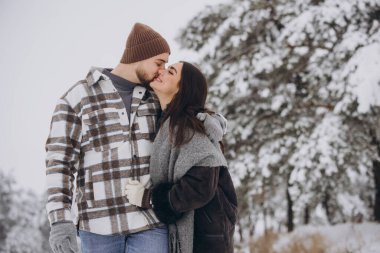 Genç, mutlu ve sevgi dolu bir çift dağlarda karlı bir ormanda yürüyor.