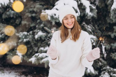 Açık havada beyaz örgü şapka, atkı, eldiven ve maytaplı süveter giyen gülümseyen kızın portresi. Noel tatili