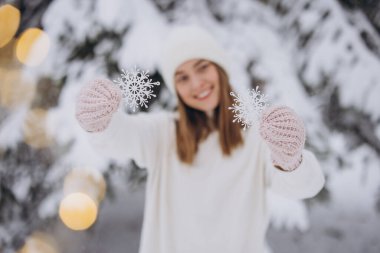 Karlı bir çam ağacının arka planında kar taneleri tutan örülü beyaz elbiseli mutlu bir kadın.