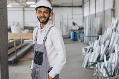 Gri üniformalı mutlu bir Hintli işçinin portresi ve fabrika yapımının arka planında poz veren beyaz bir şapka.