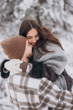 Genç, mutlu ve sevgi dolu bir çift dağlarda karlı bir ormanda yürüyor.