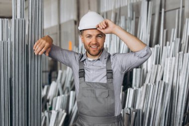 Özel üniformalı, beyaz şapkalı, sakallı, erkek fabrika işçisi metal pencere ve kapılarda alüminyum çerçeve taşıyor.